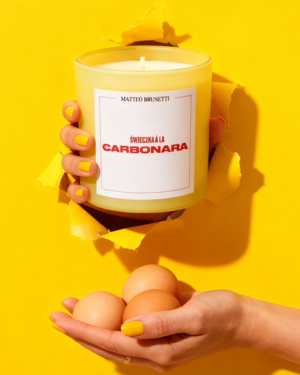 Żółta świeca A La Carbonara trzymana w dłoni, żółte tło